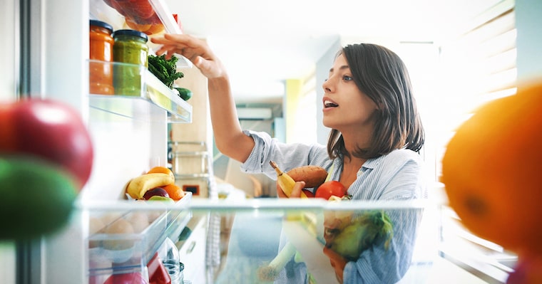 Woman choosing vegetables and ingredients from an open fridge