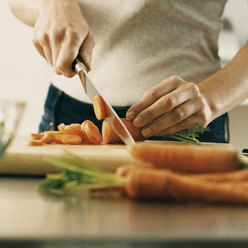 A close up image of a man slicing a carrot.